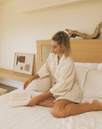 Woman reading a book on the bed wearing Lara cotton kimono.